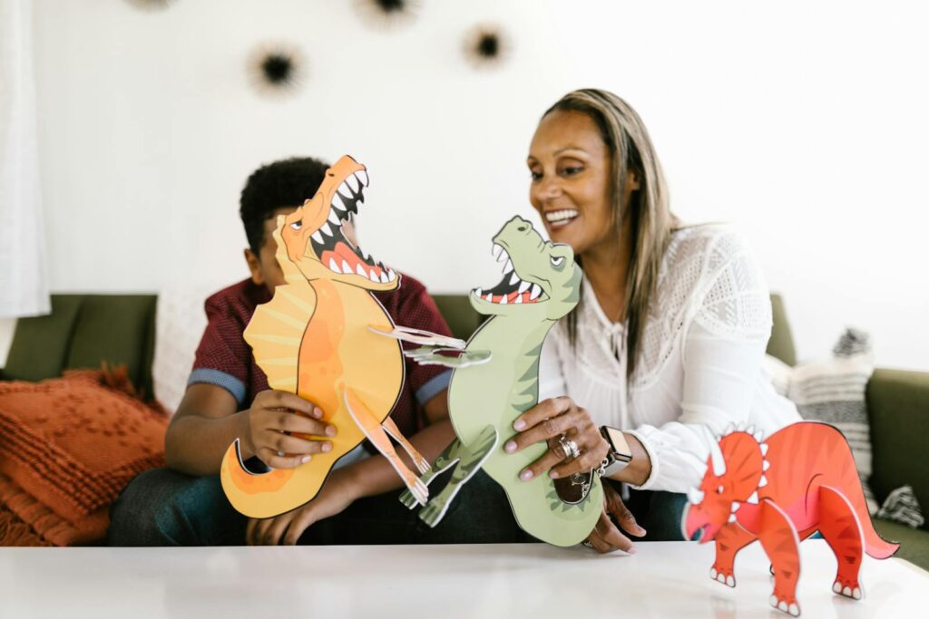 Mother and son share quality time indoors playing with dinosaur crafts, smiling and bonding.
